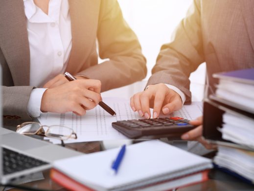 Two female accountants counting on calculator income for tax form completion hands close-up. Business and audit concept