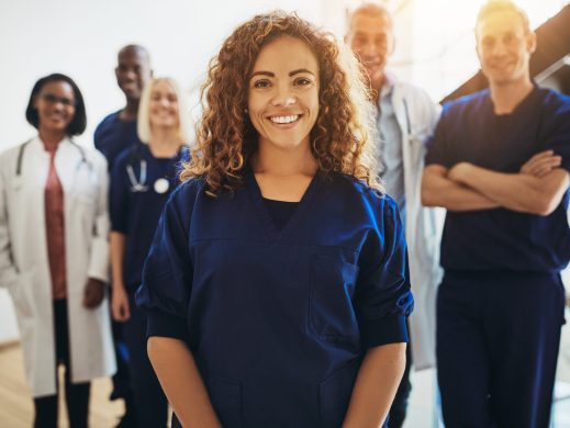 Smiling young female doctor standing in a hospital corridor with a diverse group of medical staff standing behind her